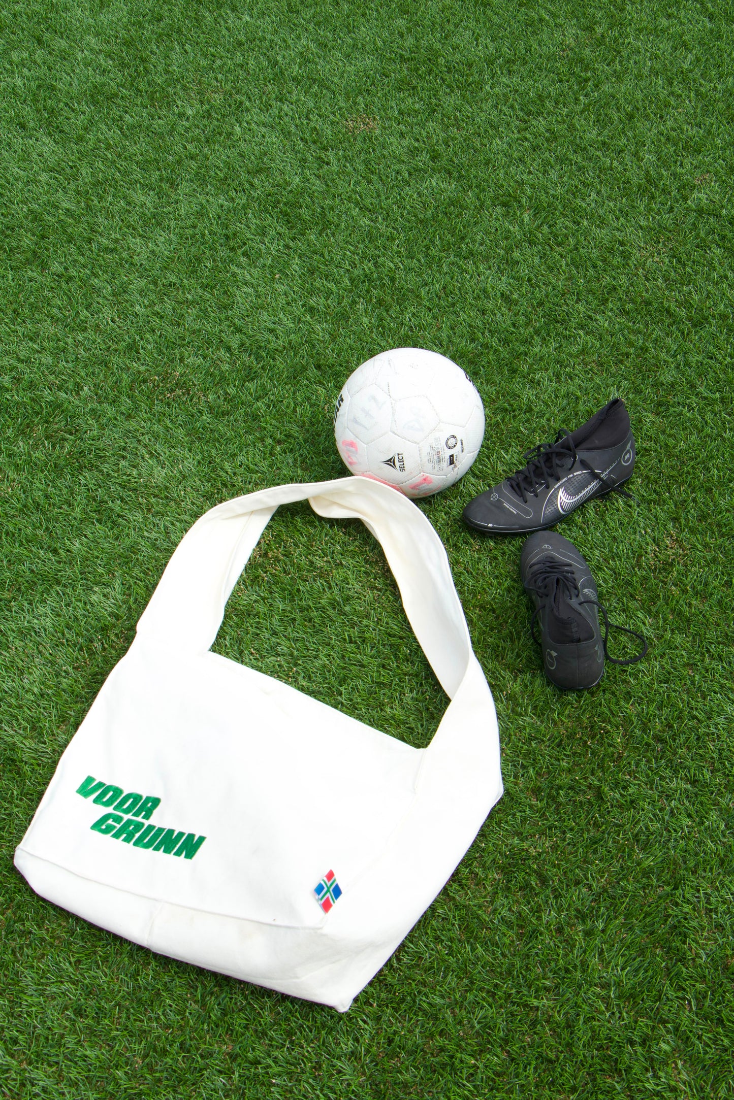 Voor Grunn Totebag op kunstgras naast een voetbal en voetbalschoenen