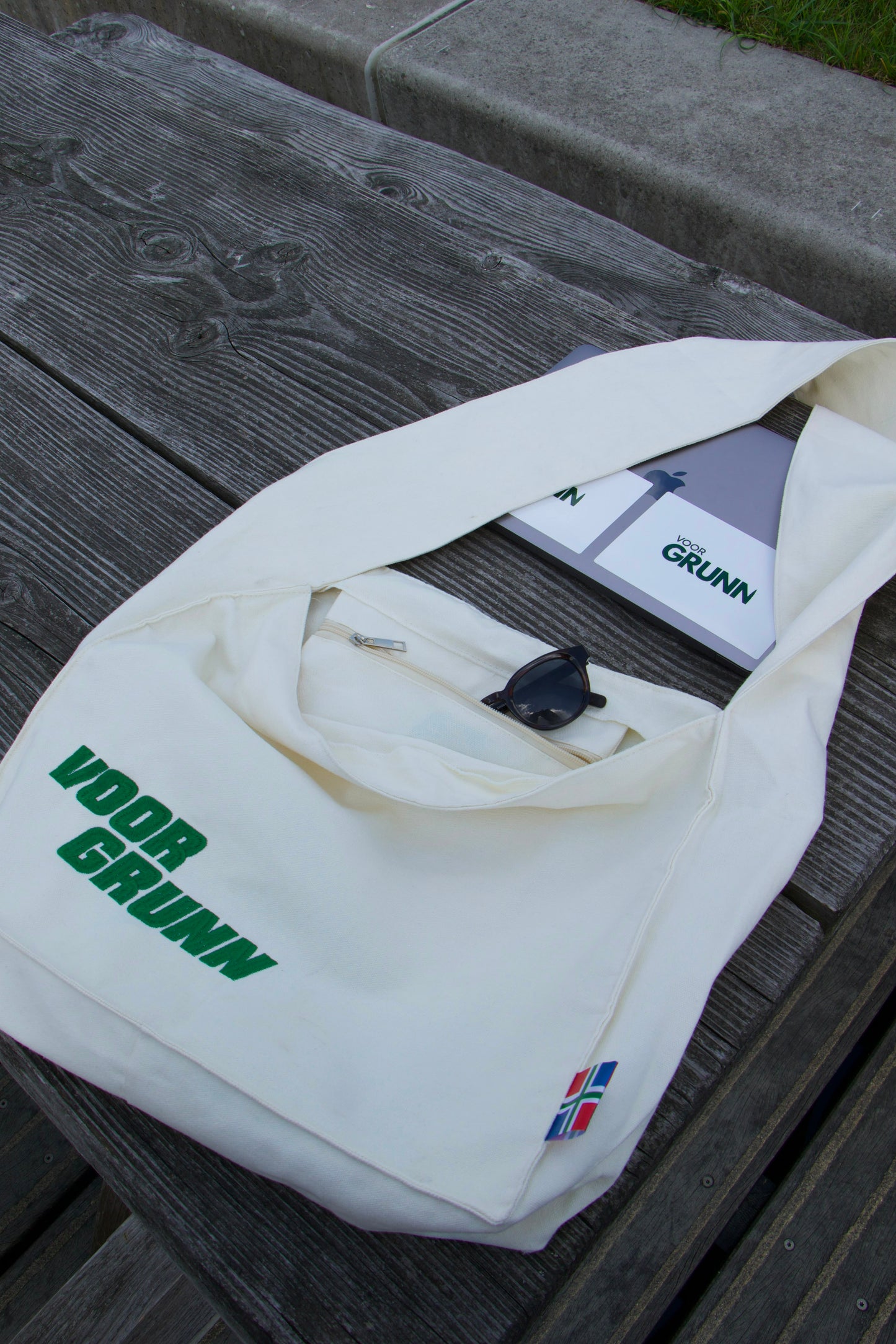 Voor Grunn Totebag met zonnebril en notitieblok erin, op een houten bank