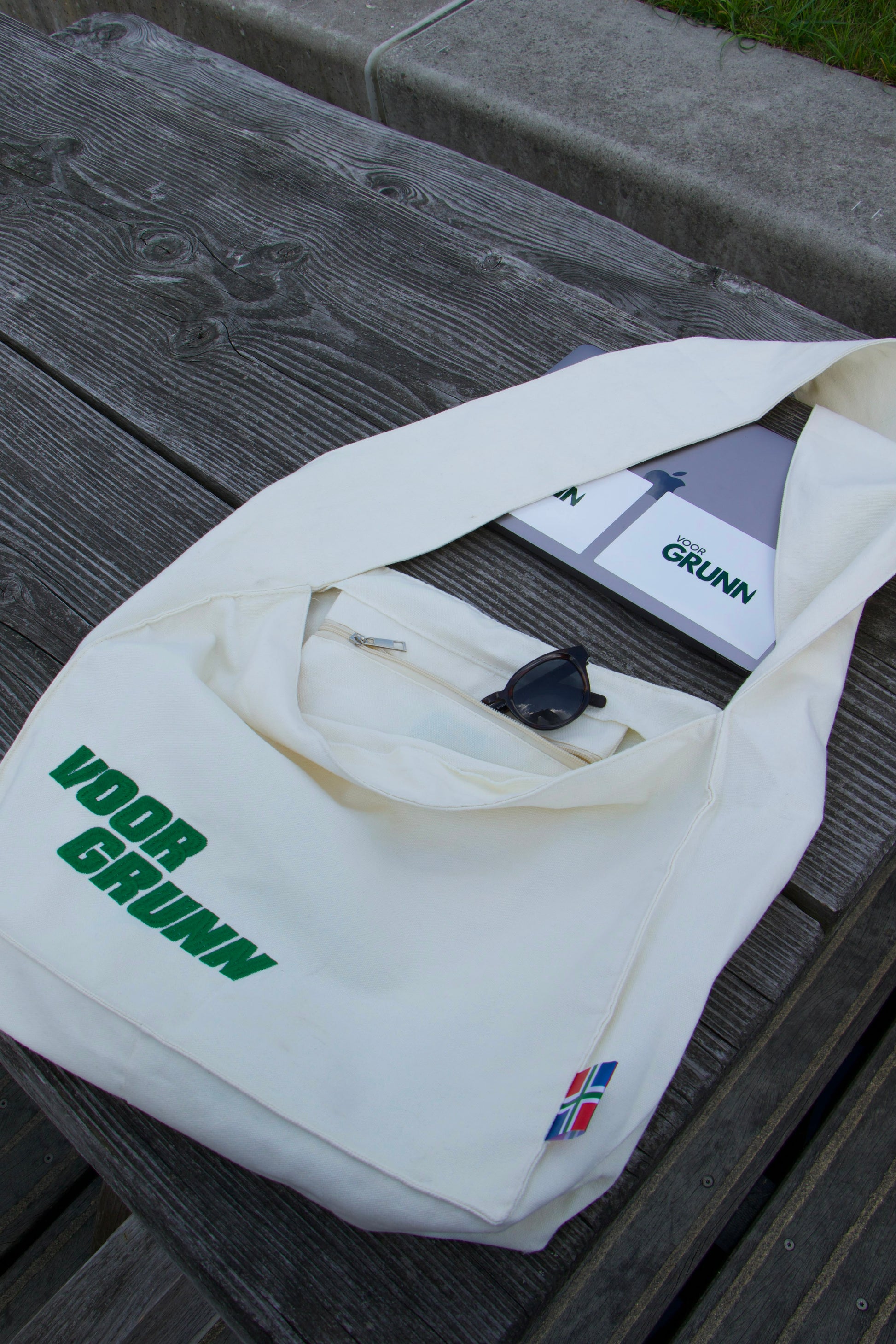 Voor Grunn Totebag met zonnebril en notitieblok erin, op een houten bank
